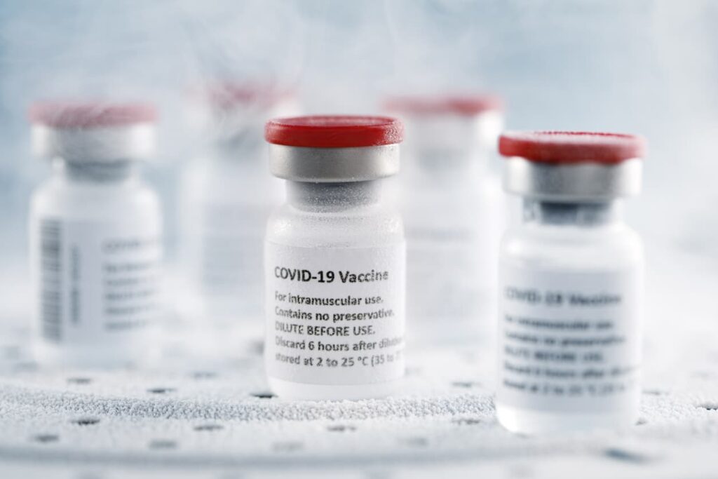 Vials of COVID-19 vaccine are shown in a frigid environment with frost.